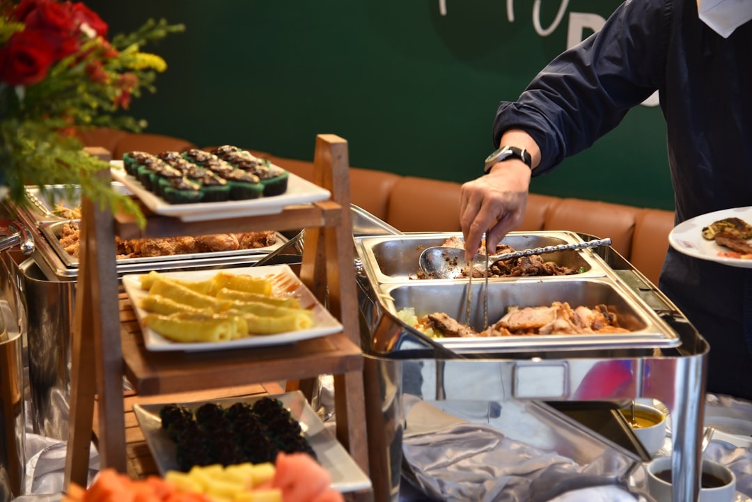 A hand uses tongs to serve meat at a buffet.